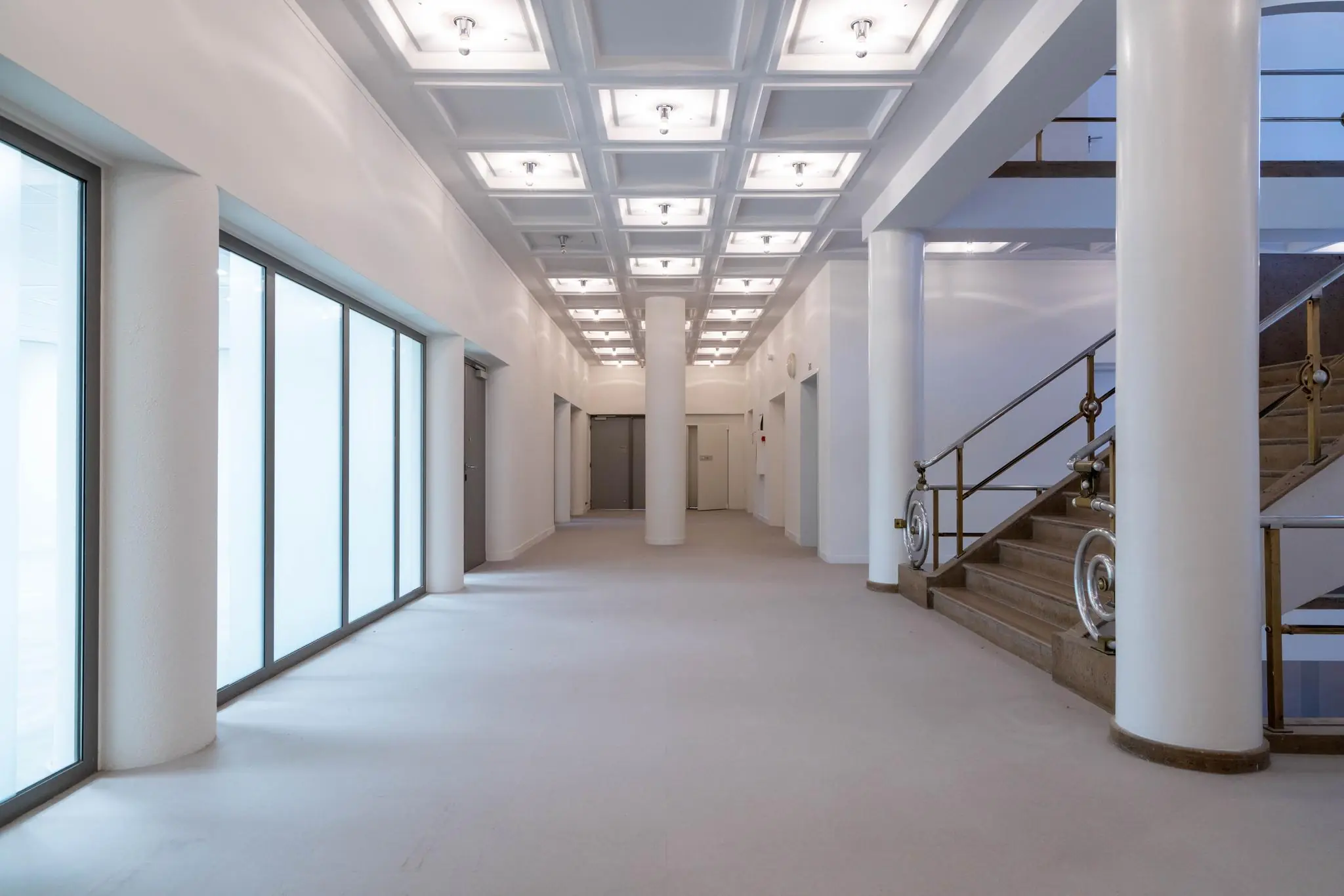 Licht en ruim interieur van een modern kantoorpand aan de Wassenaarseweg met grote ramen, witte pilaren en een trap met metalen leuning.