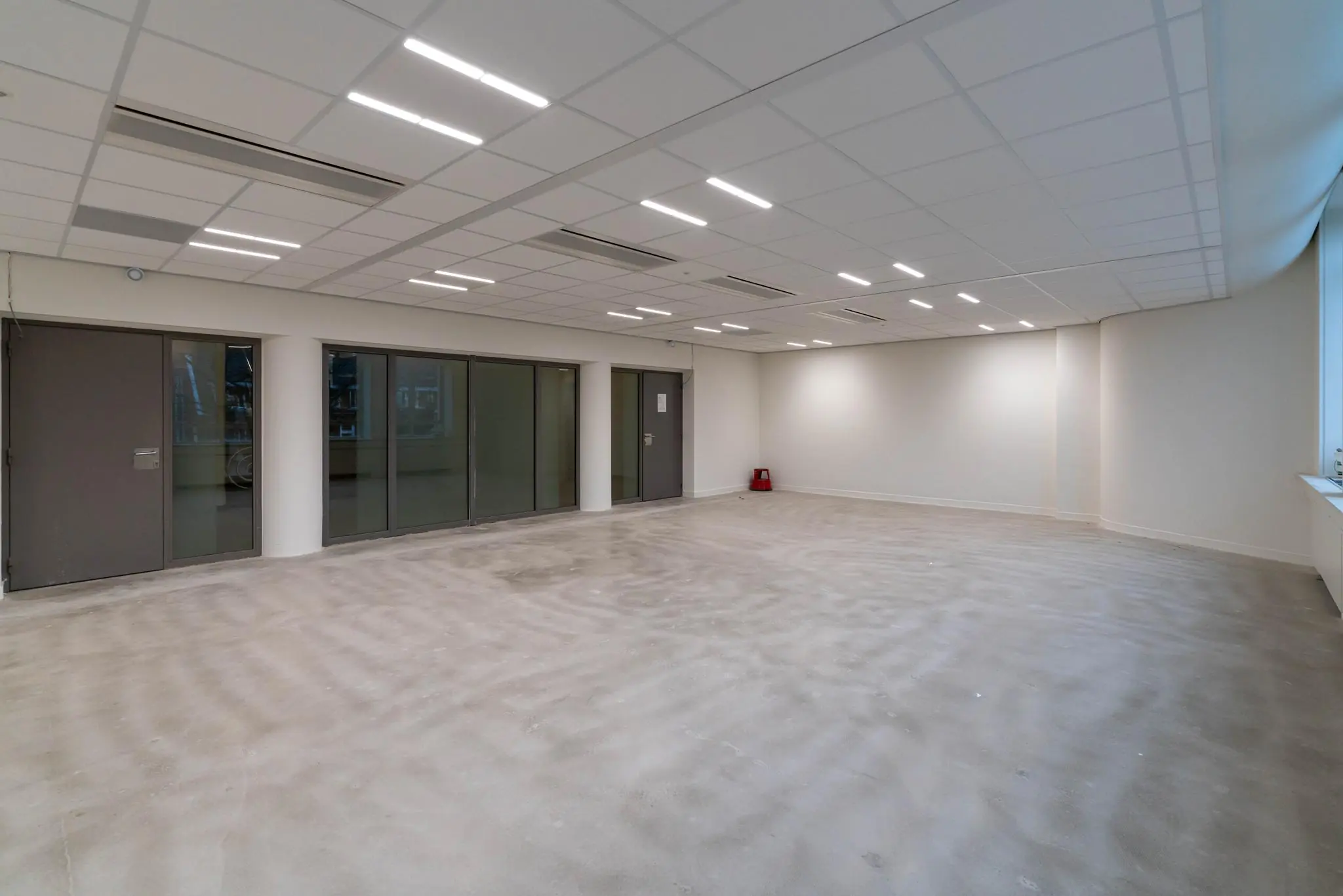 Lege, strakke kantoorruimte met systeemplafond, glazen schuifdeuren en betonnen vloer aan de Wassenaarseweg.