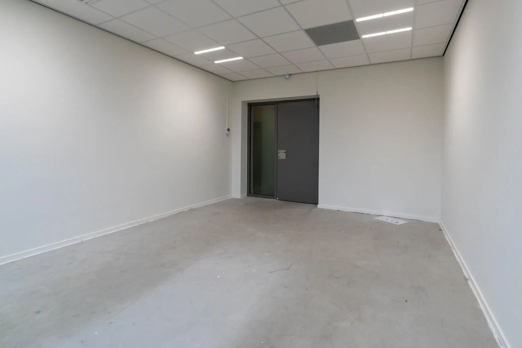 Lege, witte kantoorruimte aan de Wassenaarseweg met grijze deur en systeemplafond.