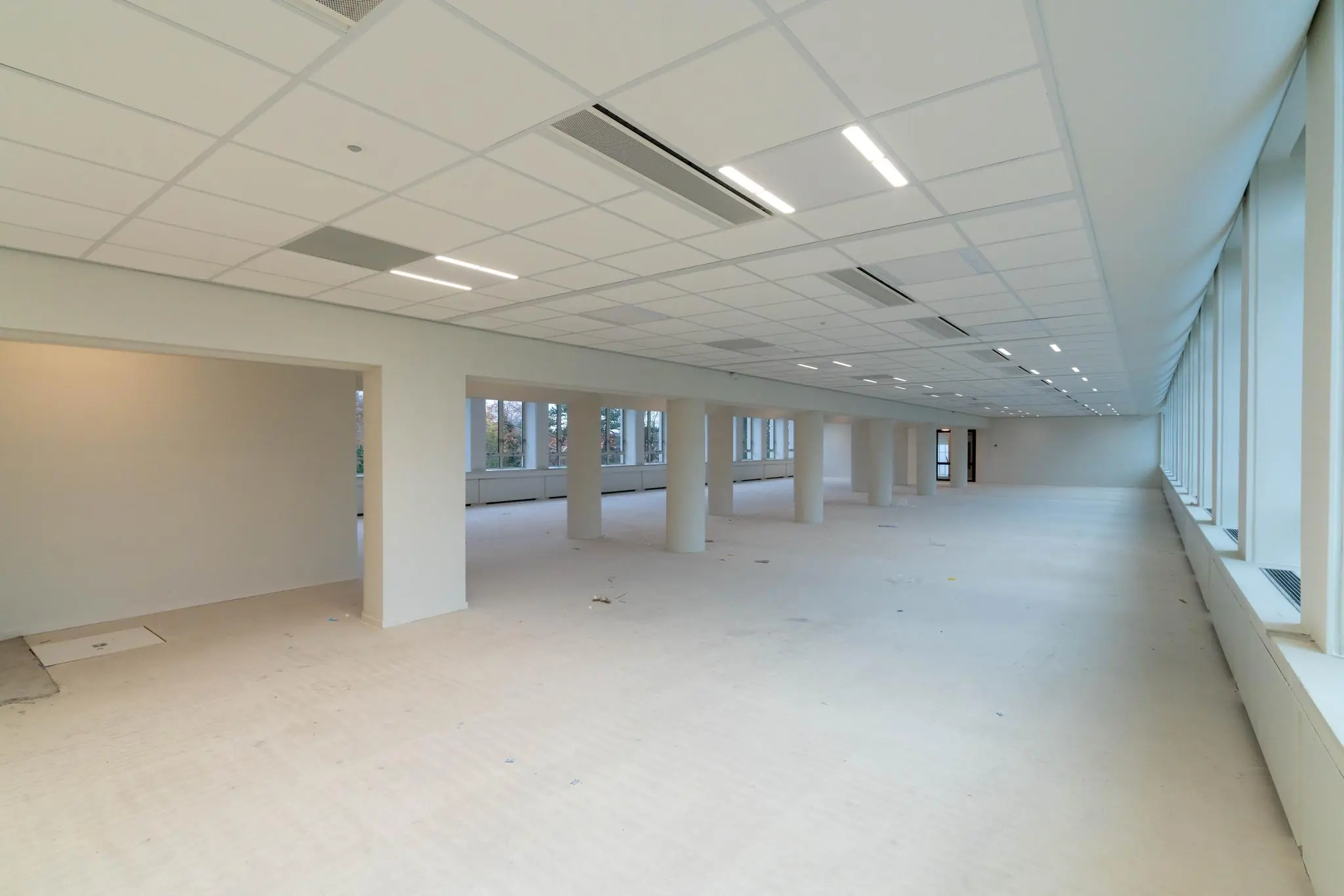 Leeg kantoorpand aan de Wassenaarseweg met witte wanden, systeemplafond en grote ramen langs de rechterzijde.