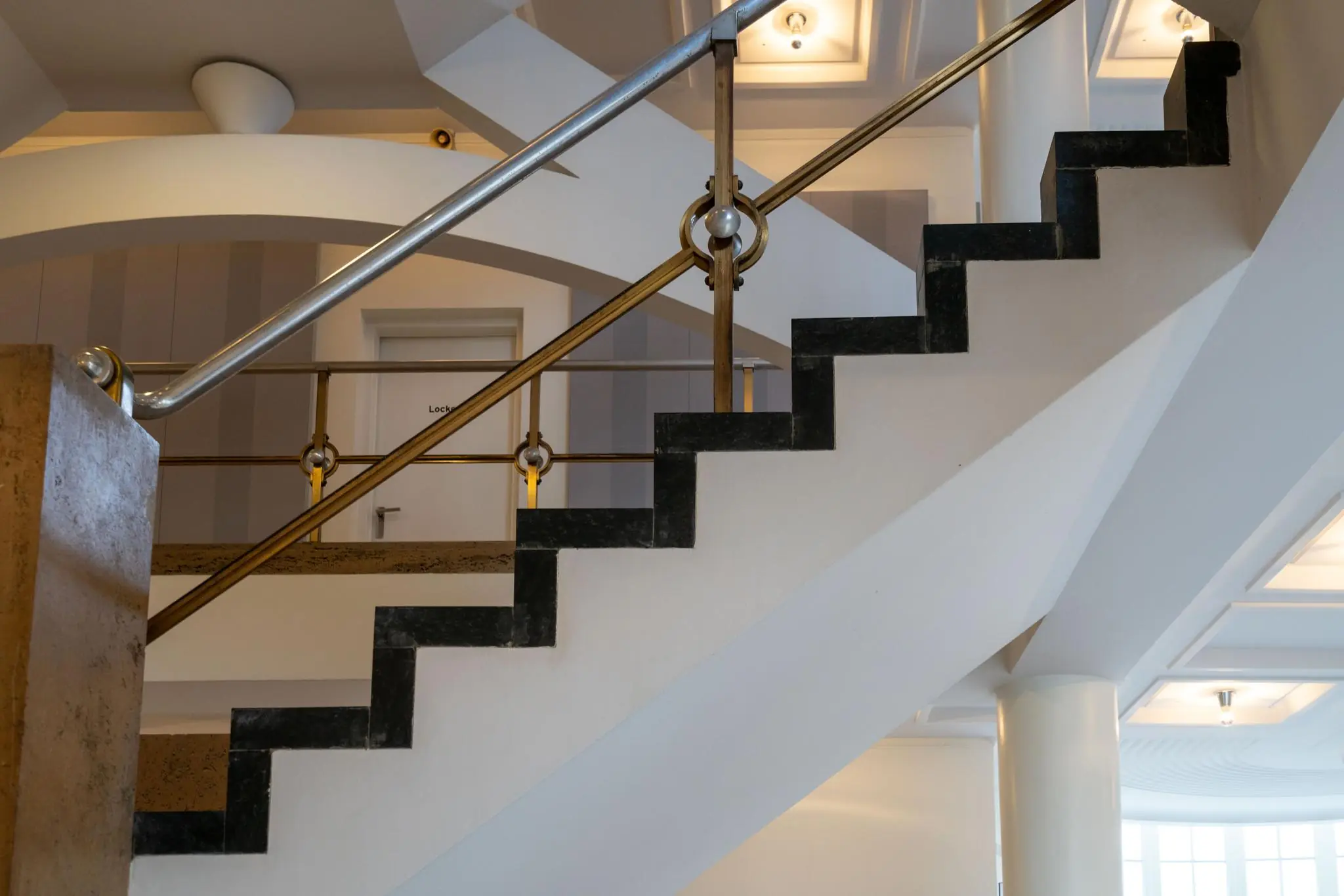 Trap met zwarte stootborden en goudkleurige leuning in een modern interieur aan de Wassenaarseweg.