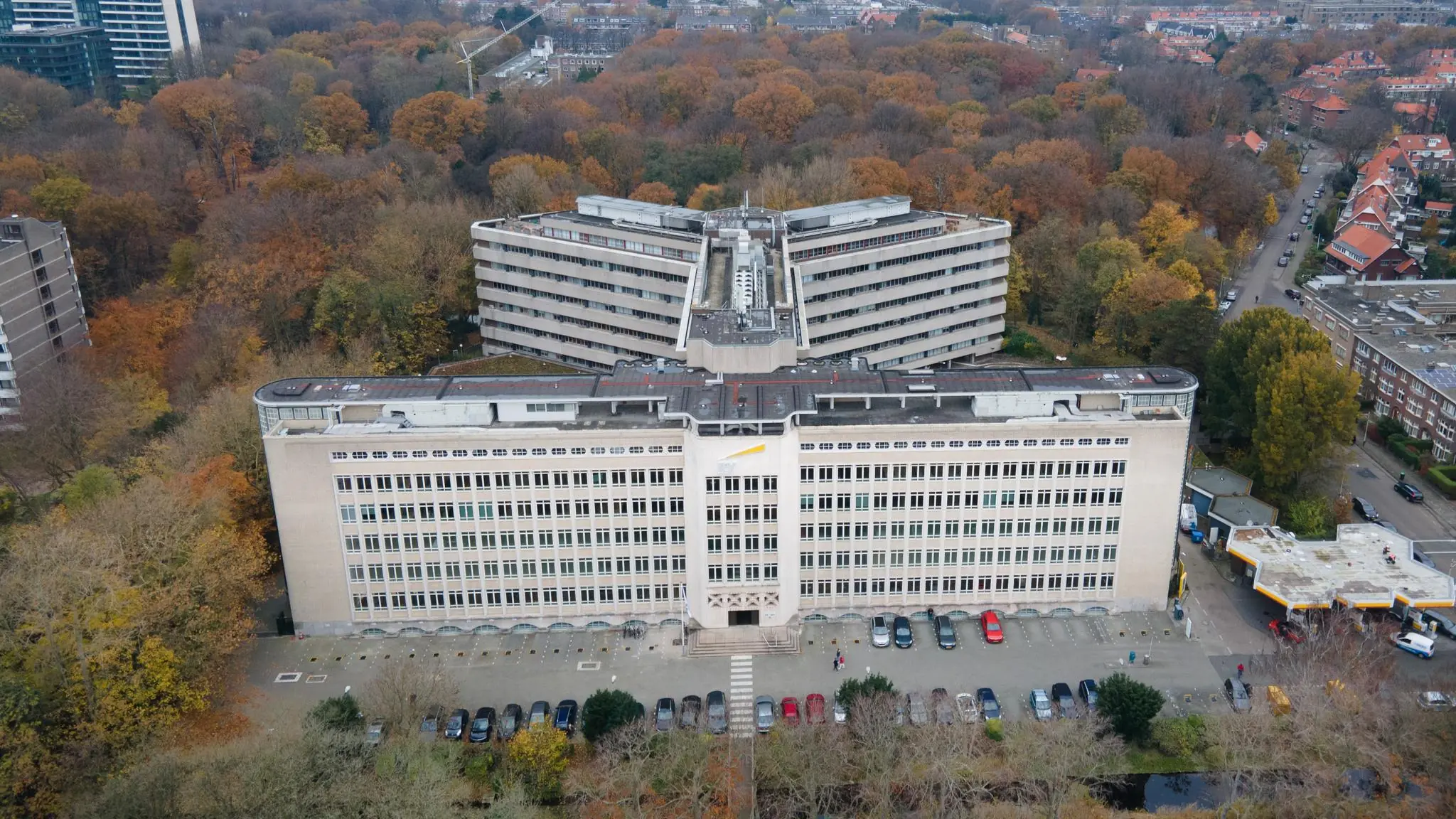 Luchtfoto van het grote kantoorgebouw aan de Wassenaarseweg in Den Haag, omringd door herfstkleurige bomen.