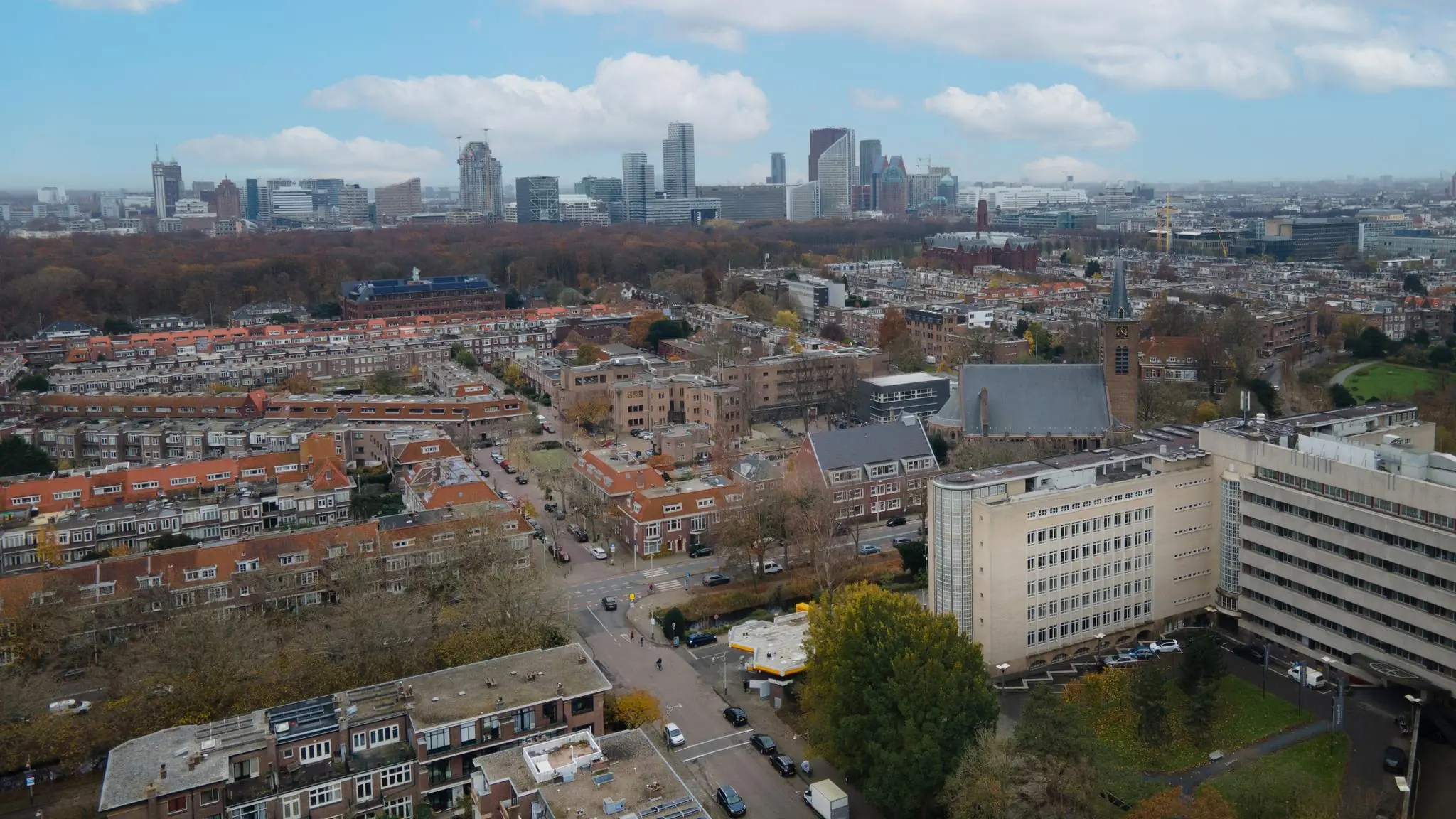 Luchtfoto van de Wassenaarseweg in Den Haag met woonwijken, een kerk, kantoorgebouwen en de skyline van de stad op de achtergrond.