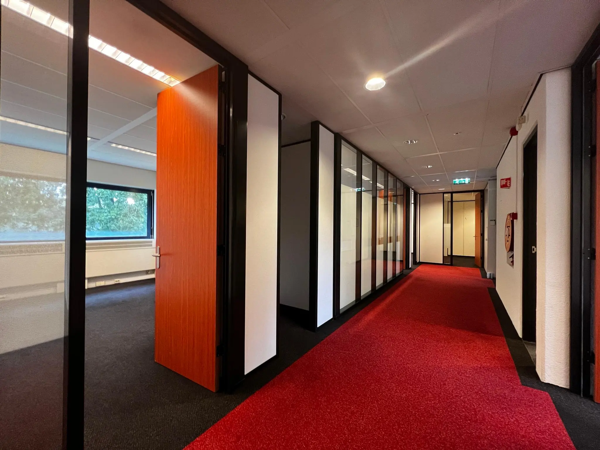Gang met rode vloerbedekking en glazen kantoorwanden aan de Vreeswijksestraatweg.