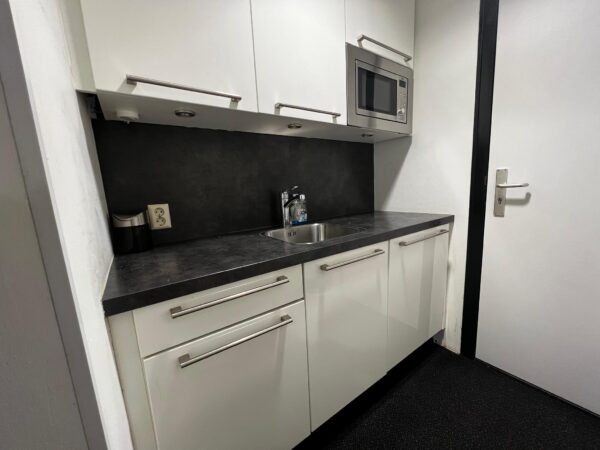 Kleine moderne kitchenette met witte kastjes, zwarte aanrechtblad, ingebouwde magnetron en een spoelbak.