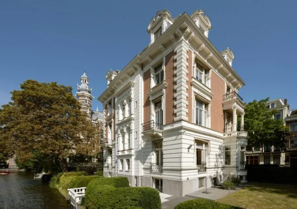 Klassiek herenhuis aan de Weteringschans in Amsterdam met uitzicht op een gracht en een historische toren op de achtergrond.