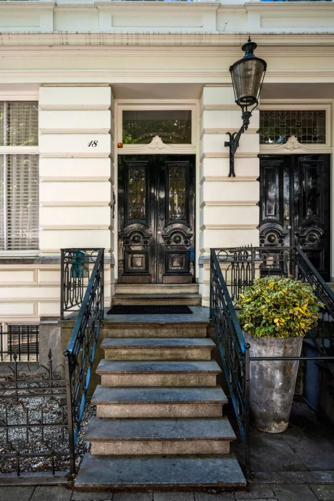 Ingang van een klassiek herenhuis aan de Weteringschans 18 met een dubbele zwarte voordeur en stenen trap met smeedijzeren hekwerk.