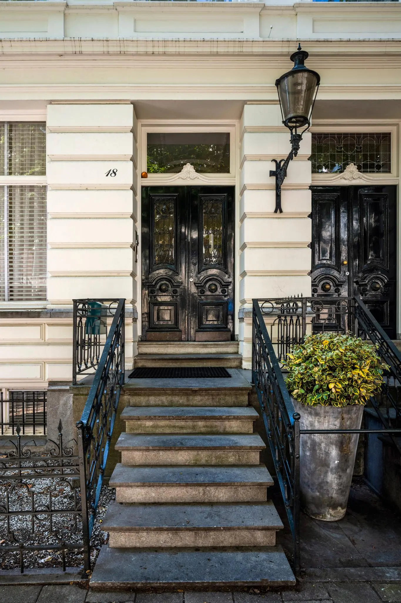 Ingang van een klassiek herenhuis aan de Weteringschans 18 met een dubbele zwarte voordeur en stenen trap met smeedijzeren hekwerk.