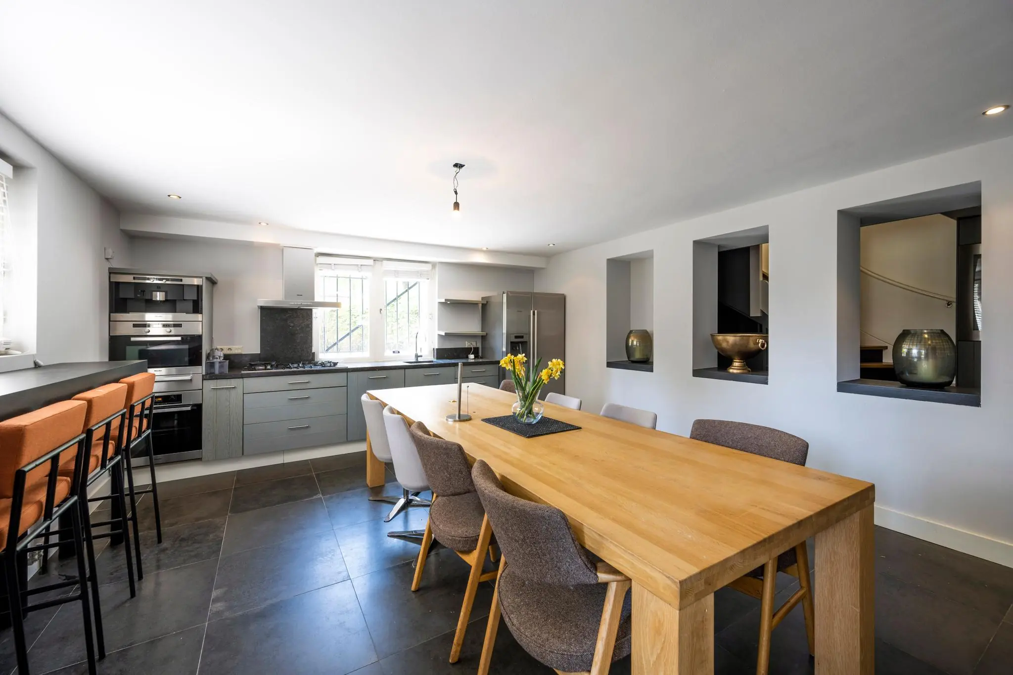 Moderne open keuken aan de Weteringschans met een houten eettafel, grijze keukenkasten en grote raampartijen.