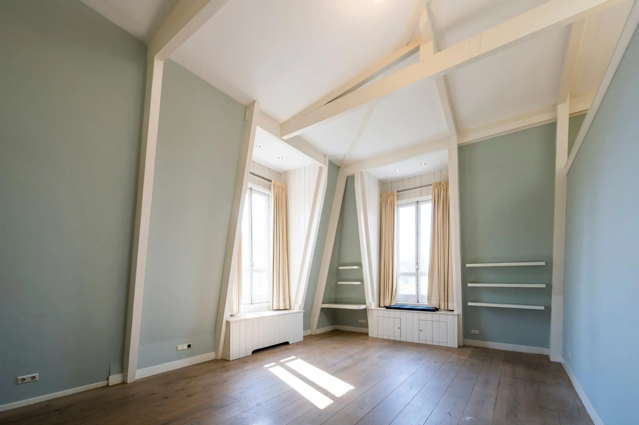 Licht en ruim vertrek aan de Weteringschans met hoge plafondbalken, grote ramen en ingebouwde wandplanken.