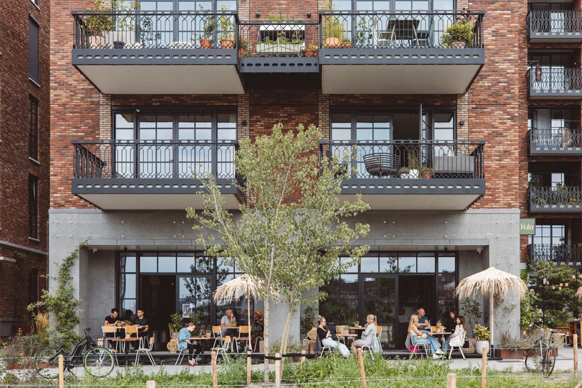 Een modern appartementencomplex met een terras waar mensen buiten zitten onder parasols.
