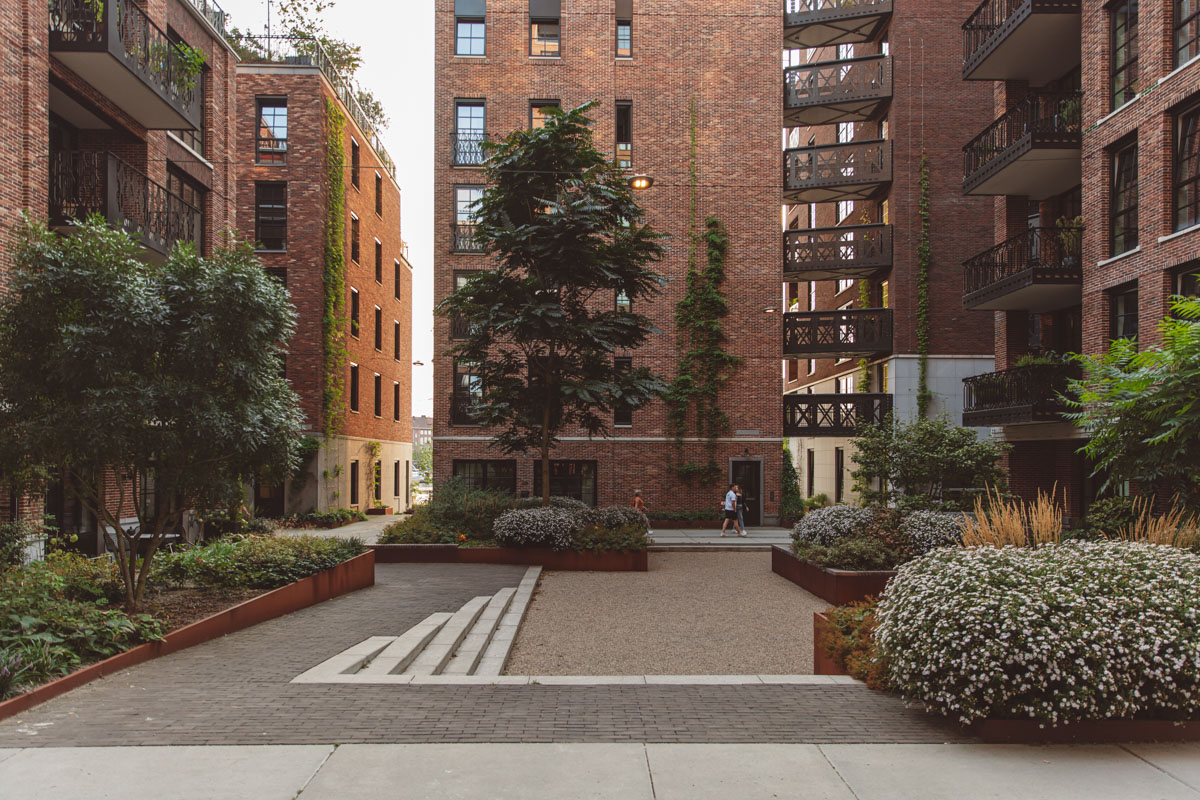 Een rustig binnenplein omringd door bakstenen woongebouwen met groene beplanting.