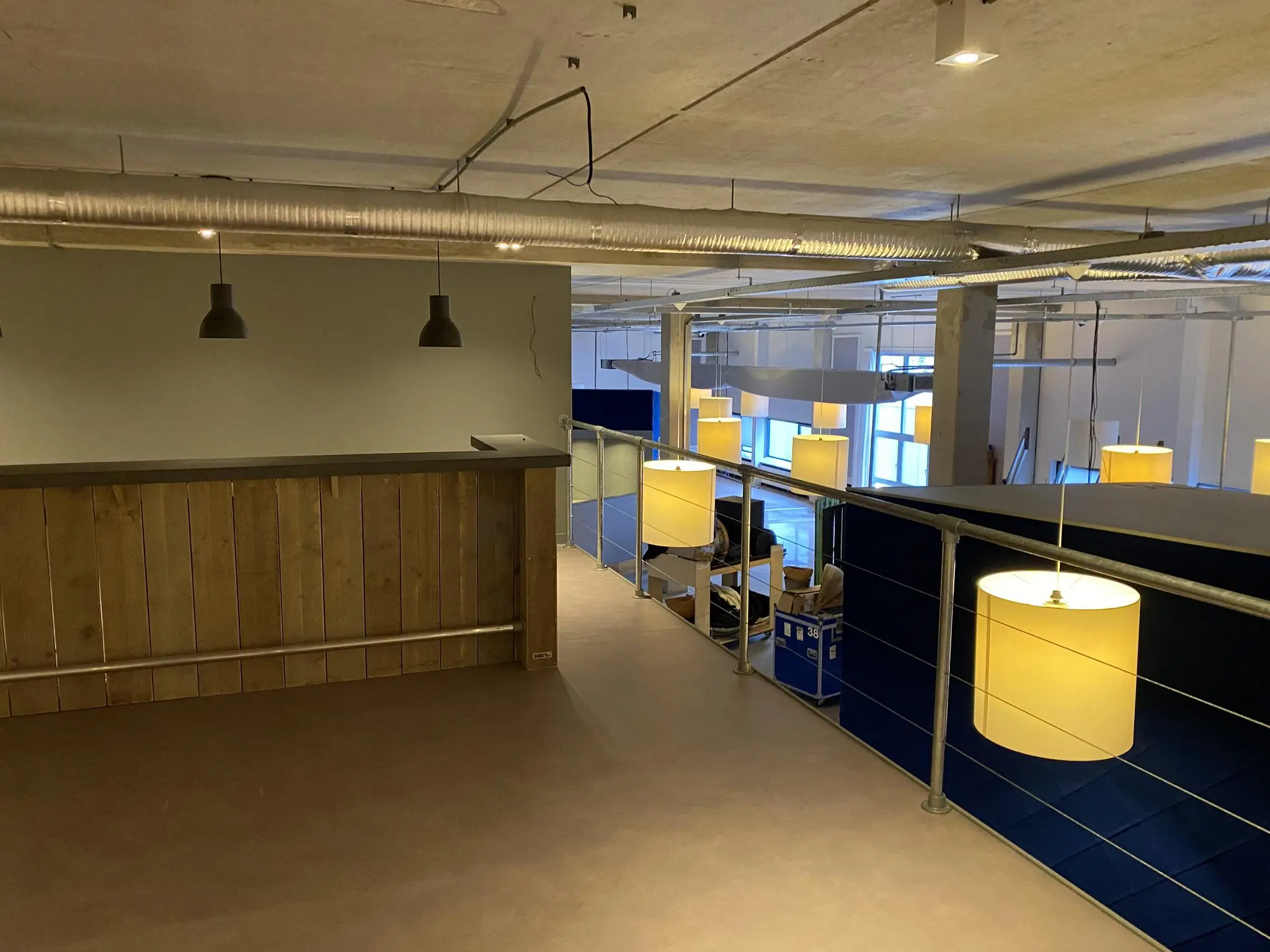 Kantoorruimte aan de Lulofsstraat met een houten bar, industriële plafondbuizen en hanglampen, gezien vanaf een bovenverdieping.