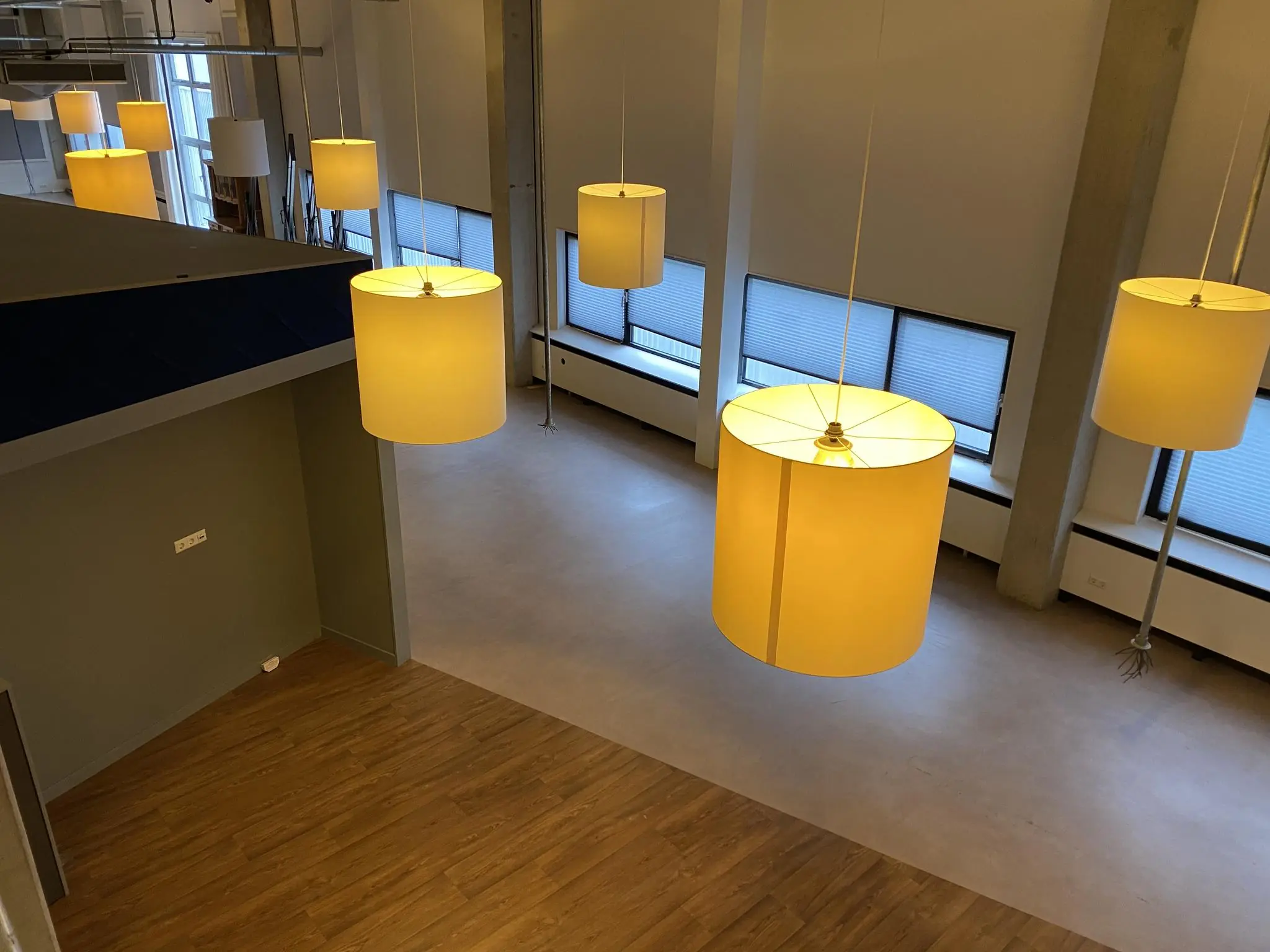 Binnenruimte aan de Lulofsstraat met grote hanglampen, houten vloer en hoge ramen met zonwering.