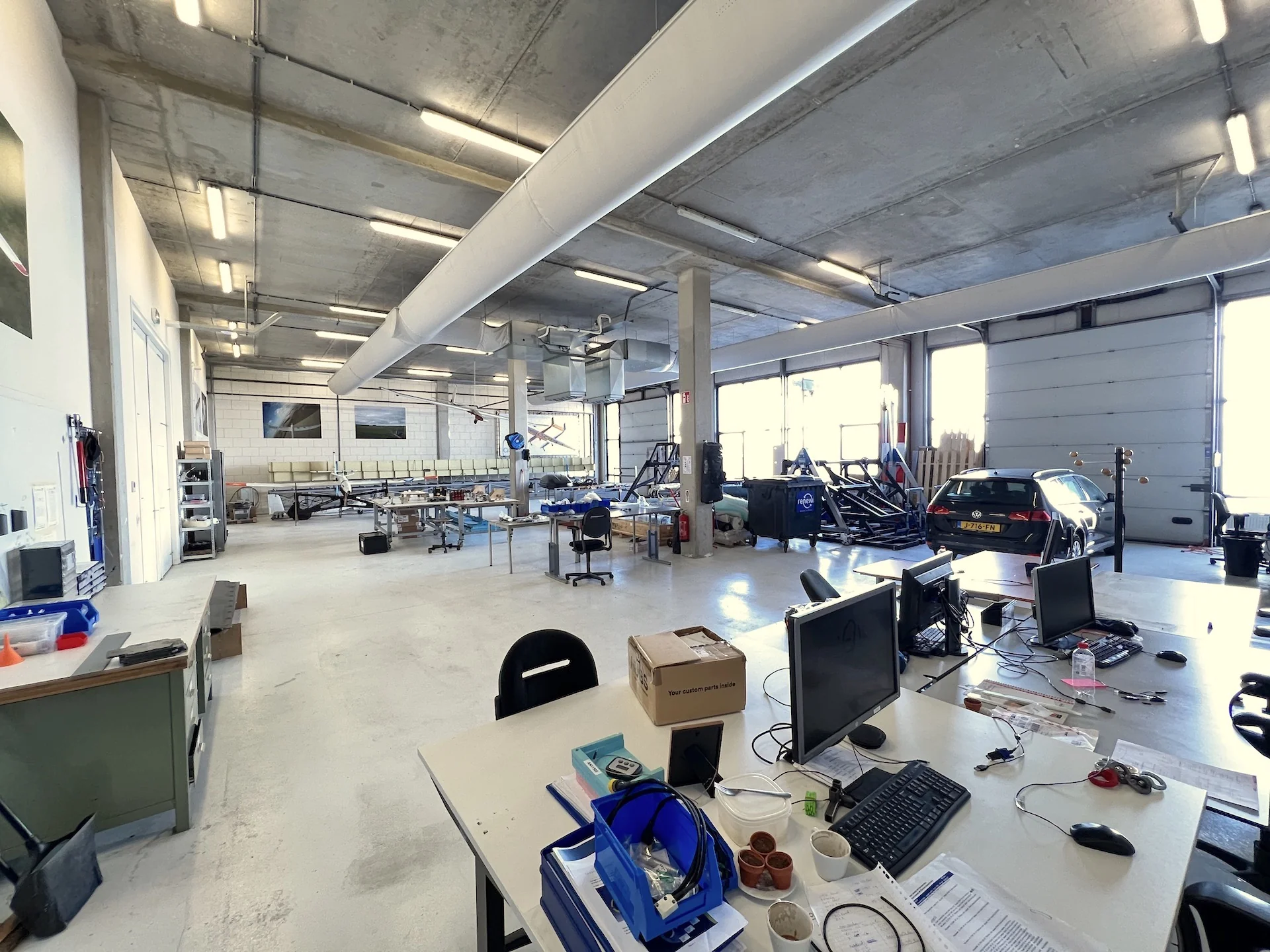 Ruime werkplaats aan de Lulofsstraat met werkbanken, computers, een auto en vliegtuigonderdelen.