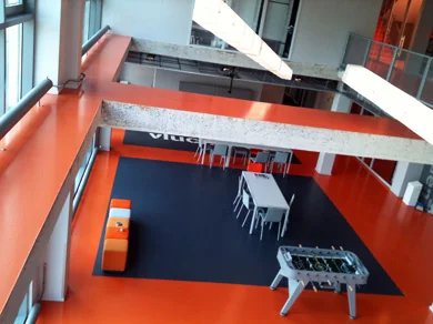 Moderne gemeenschappelijke ruimte aan de Lulofsstraat met feloranje vloer, zithoeken, tafels en een tafelvoetbaltafel.