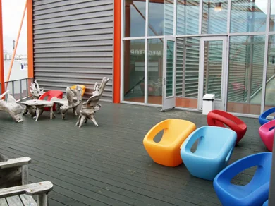 Buitenterras aan de Lulofsstraat met kleurrijke moderne stoelen en houten zitmeubels bij een glazen gevel.