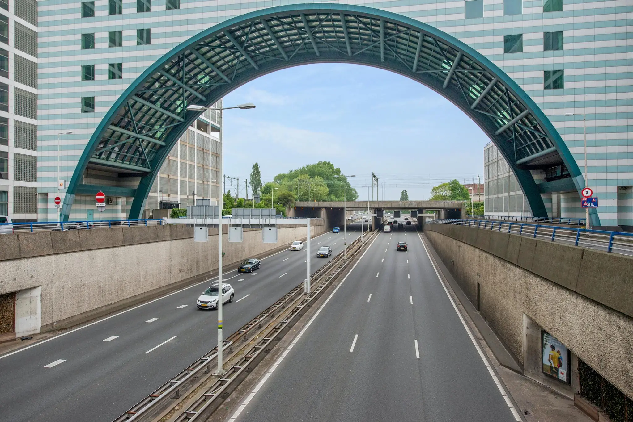 Drukke snelweg bij de Schenkkade in Den Haag met een opvallende boogconstructie tussen twee kantoorgebouwen.