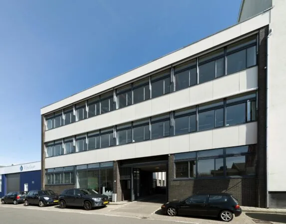 Modern kantoorgebouw aan de Helicopterstraat met grote ramen en geparkeerde auto's ervoor.