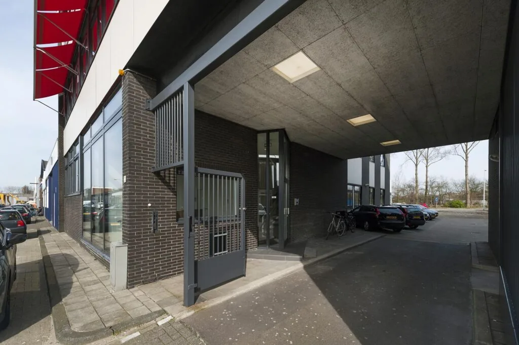 Ingang van een modern bedrijfspand aan de Helicopterstraat met parkeerruimte en fietsenstalling onder een overkapping.