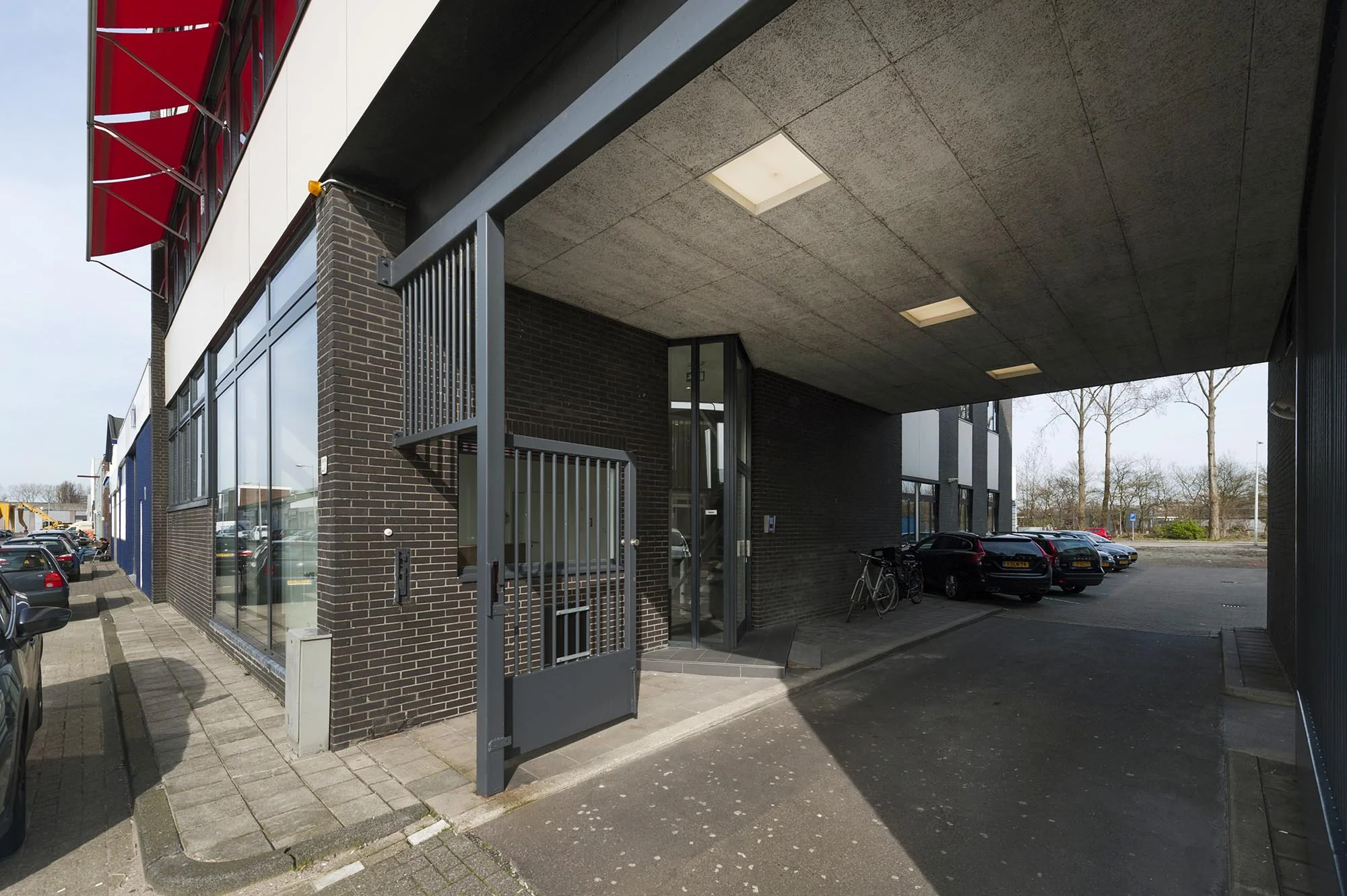 Ingang van een modern bedrijfspand aan de Helicopterstraat met parkeerruimte en fietsenstalling onder een overkapping.