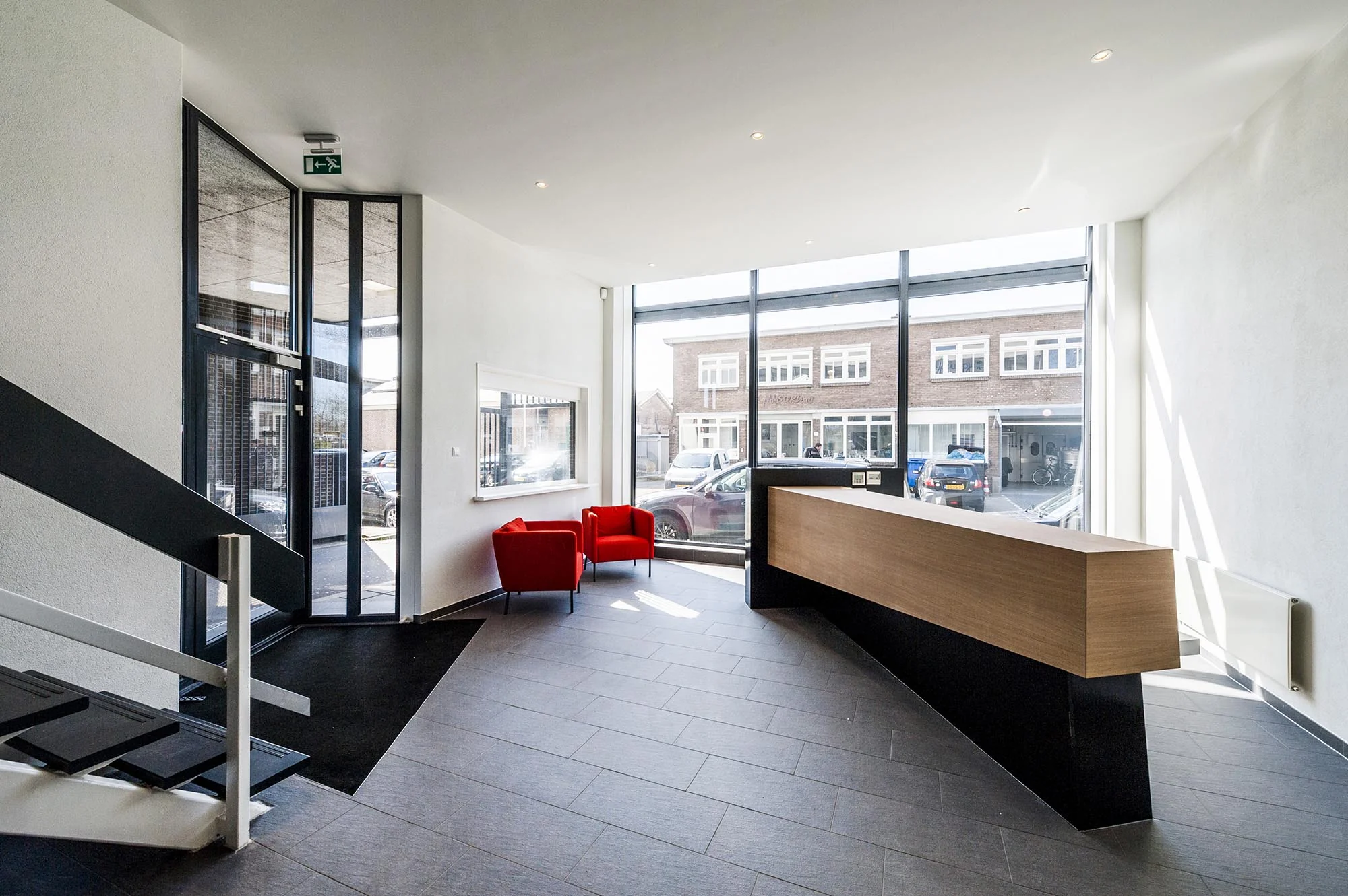 Moderne ontvangsthal aan de Helicopterstraat met houten balie, twee rode stoelen en veel daglicht via grote ramen.