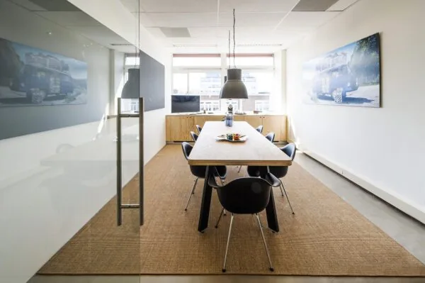 Vergaderruimte met houten tafel, zwarte stoelen en foto's van een versierde bus aan de muur in een kantoor aan de Helicopterstraat.