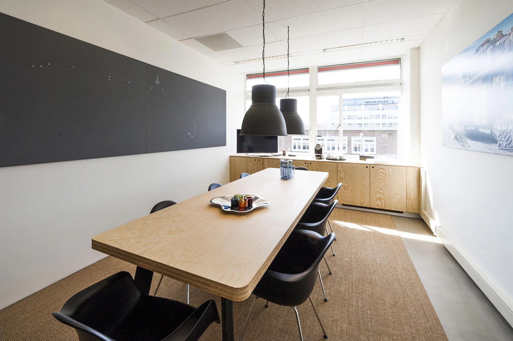 Moderne vergaderruimte aan de Helicopterstraat met houten tafel, zwarte stoelen en grote hanglampen.