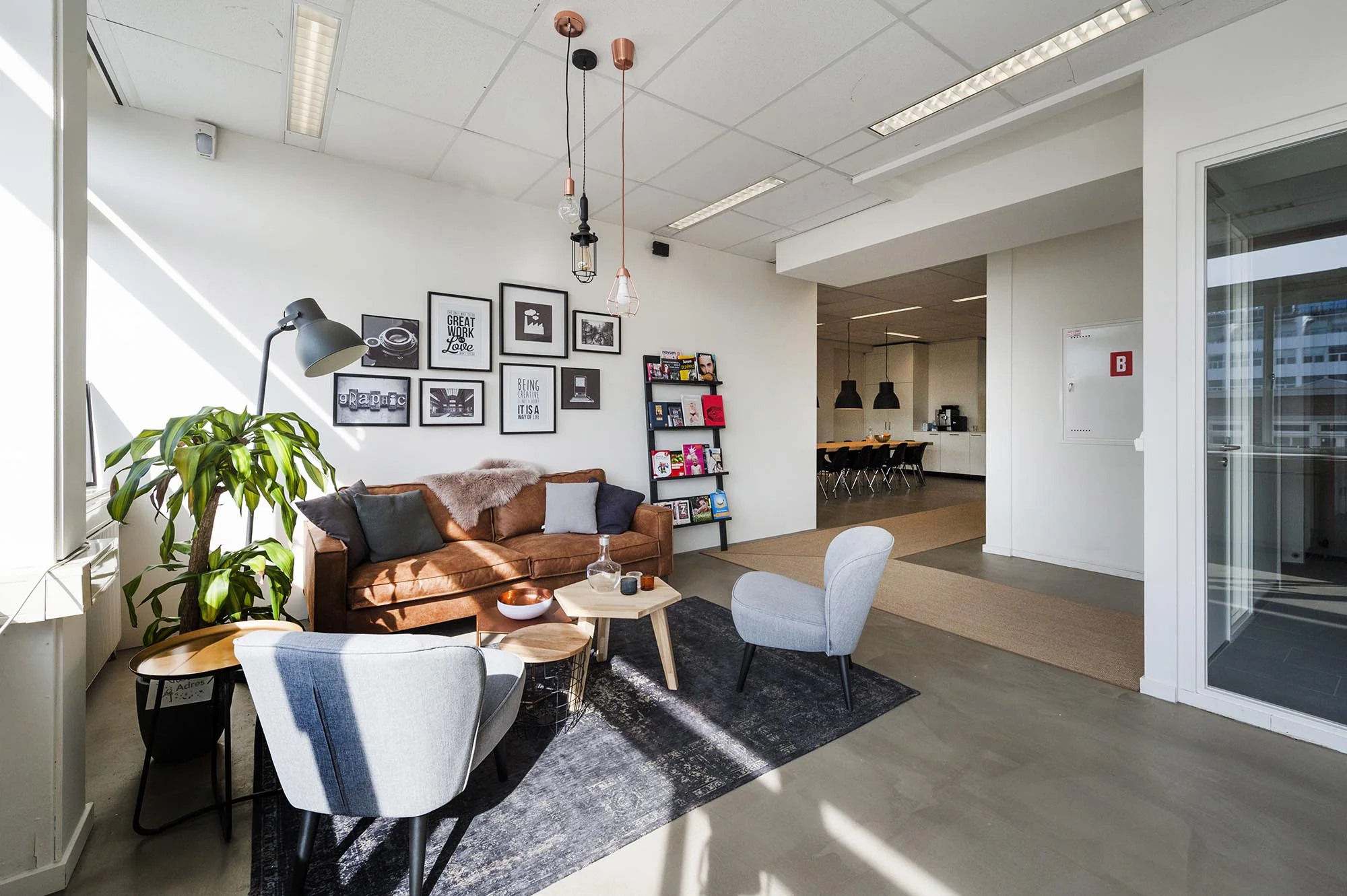 Moderne en sfeervolle kantoorlounge aan de Helicopterstraat met zithoek, kunst aan de muur en zicht op een open keukenruimte.