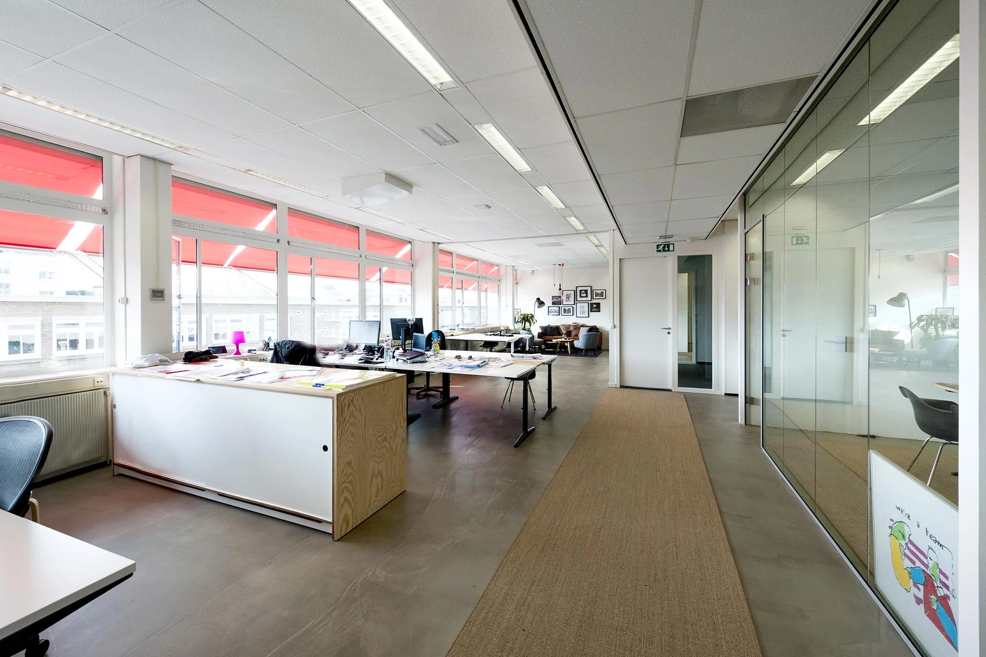 Modern kantoorinterieur aan de Helicopterstraat met open werkplekken, glazen vergaderruimte en rode zonwering.