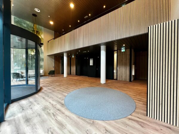 Moderne entreehal met houten vloer, ronde draaideur en zitgedeelte met stoelen.
