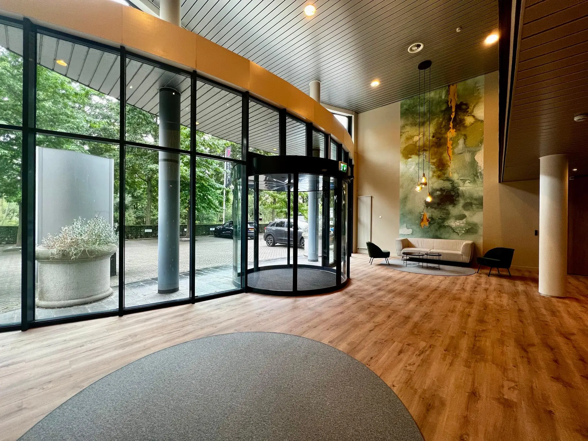 Moderne hotellobby met een glazen draaideur, houten vloer en een zithoek met kunst aan de muur.