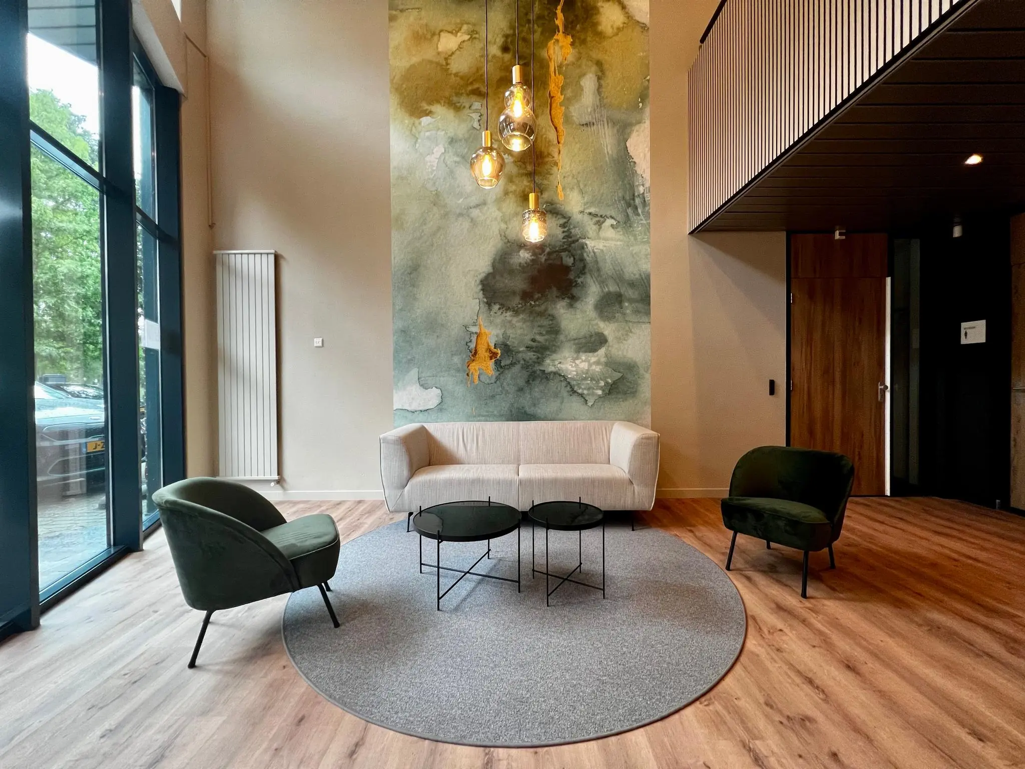 Moderne wachtruimte met een beige bank, groene stoelen, ronde tafels en kunst aan de wand.