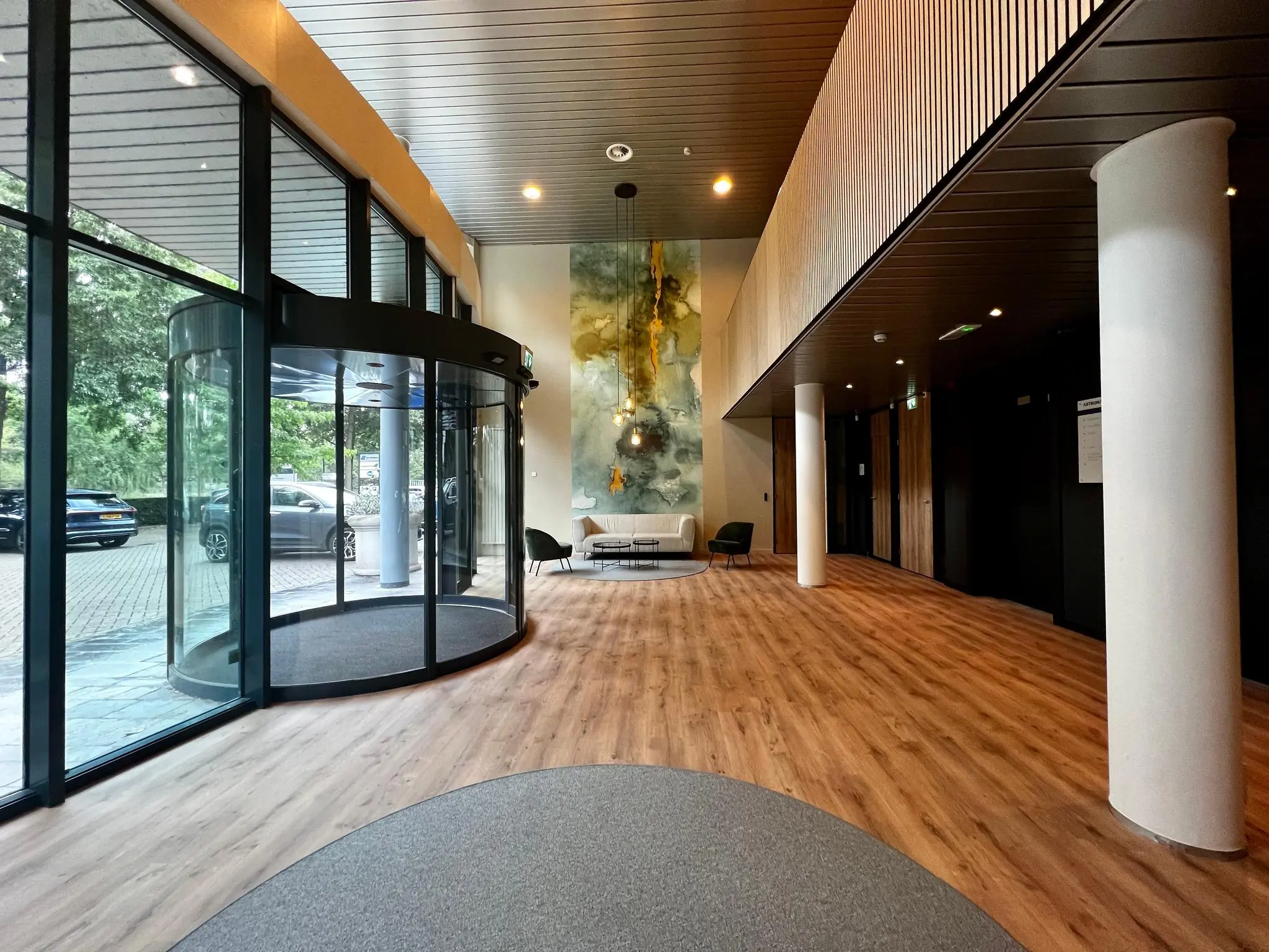 Moderne kantoorlobby met houten vloer, glazen draaideur en een muurschildering van een astronaut.
