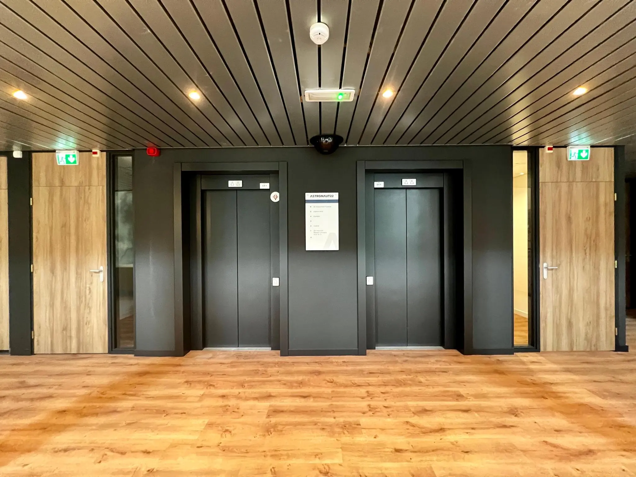 Twee liften in een modern kantoorgebouw met houten vloer en deuren, onder het naambord "ASTRONAUT".