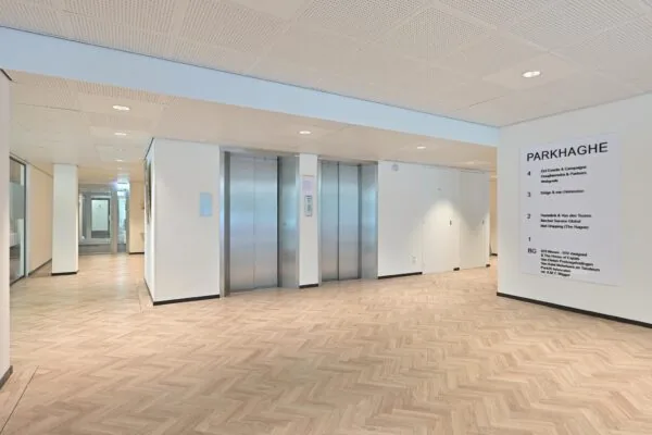 Moderne kantoorhal van het gebouw ParkHaghe met twee liften en een informatiebord aan de muur.