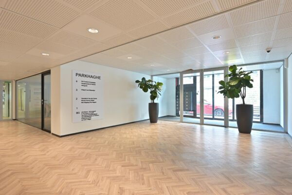 Moderne entreehal van kantoorgebouw ParkHaghe met houten visgraatvloer, glazen deuren en grote plantenbakken.