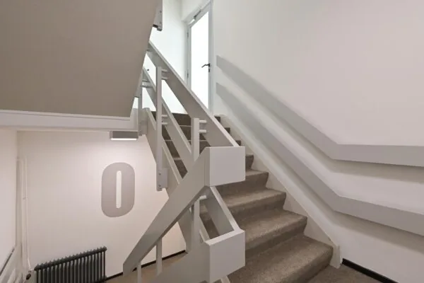 Trappenhuis met beige tapijt, witte leuningen en een deur bovenaan, gelegen op de begane grond van een gebouw aan de Parkstraat.
