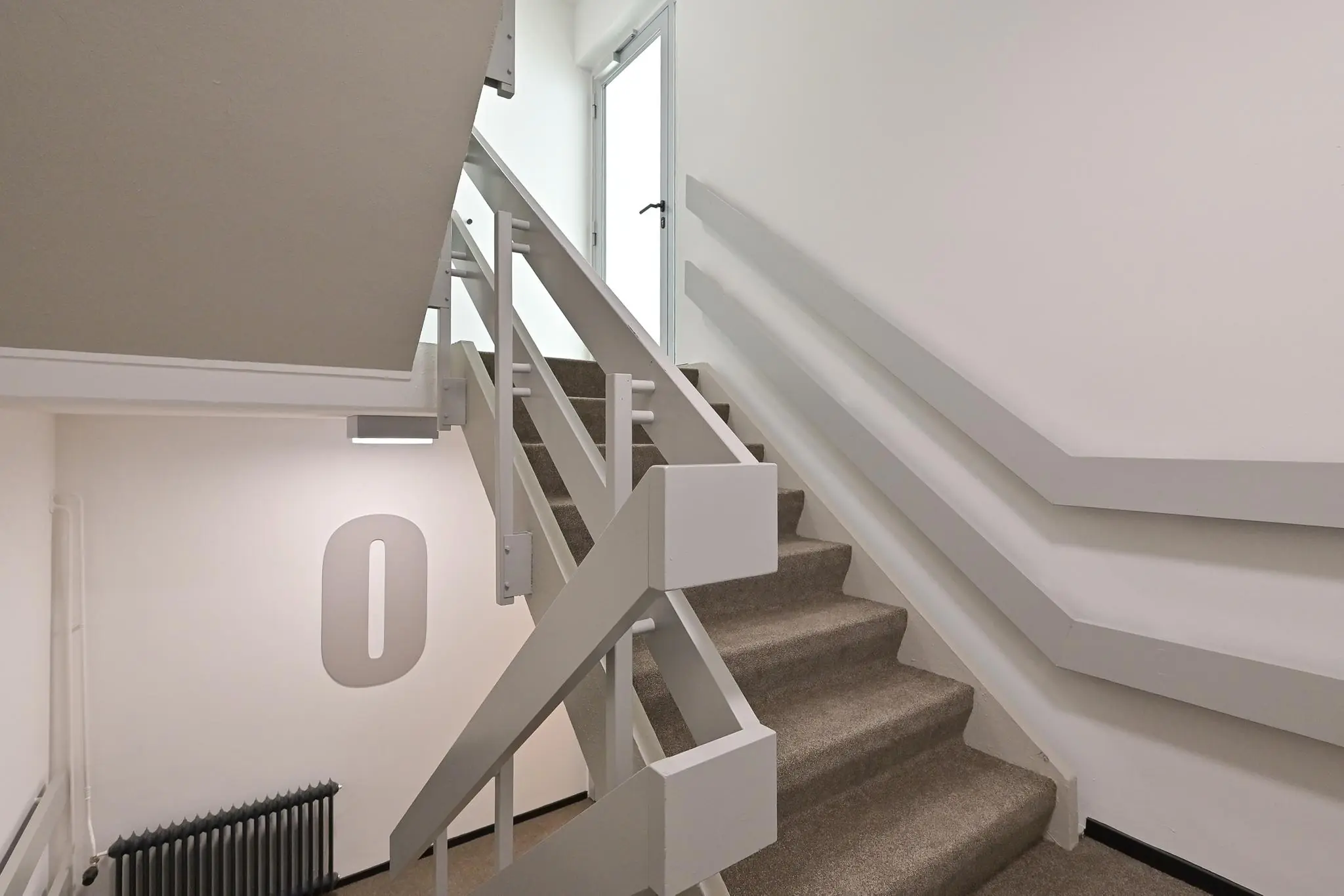 Trappenhuis met beige tapijt, witte leuningen en een deur bovenaan, gelegen op de begane grond van een gebouw aan de Parkstraat.