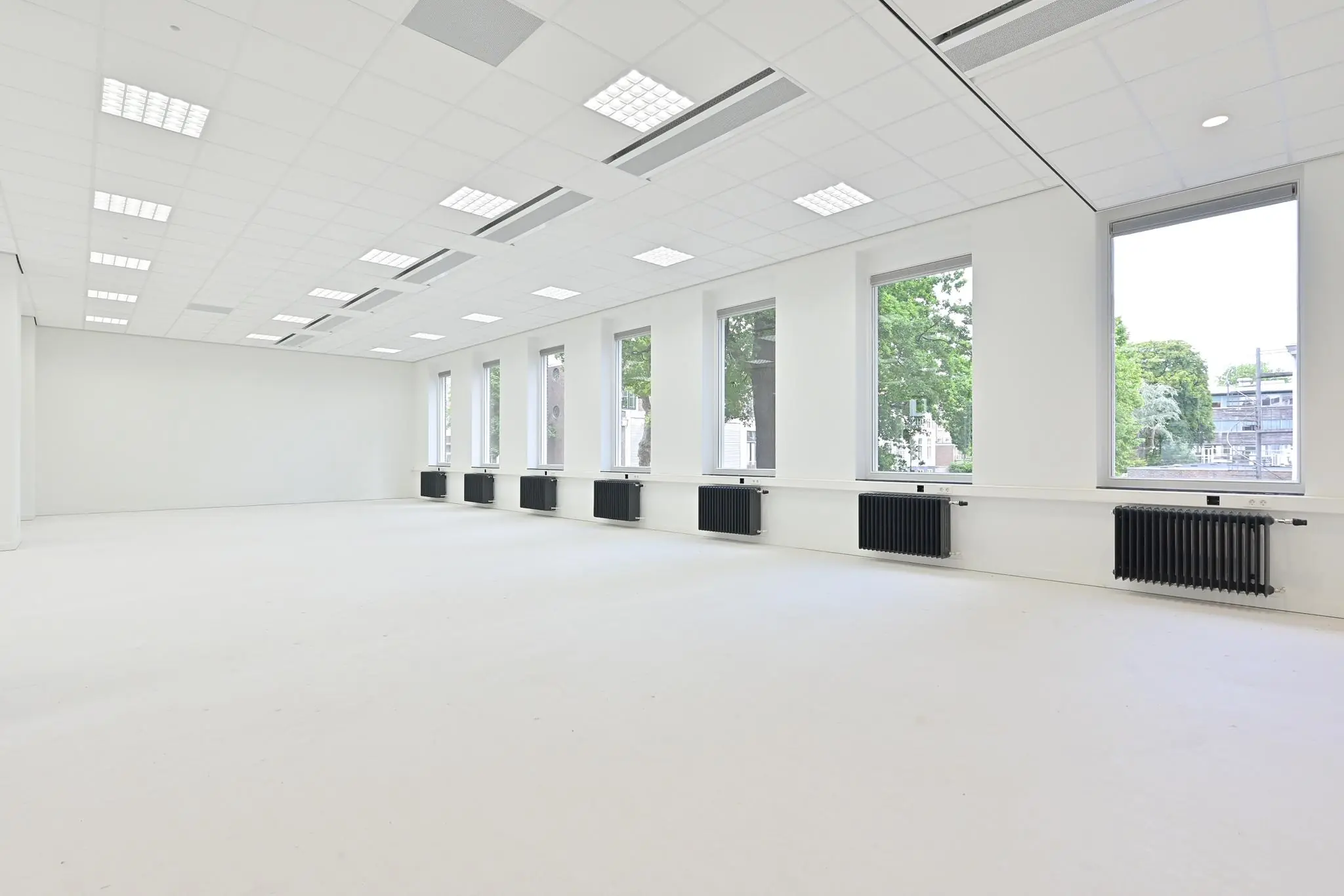Lichte, lege kantoorruimte aan de Parkstraat met grote ramen en zwarte radiatoren.