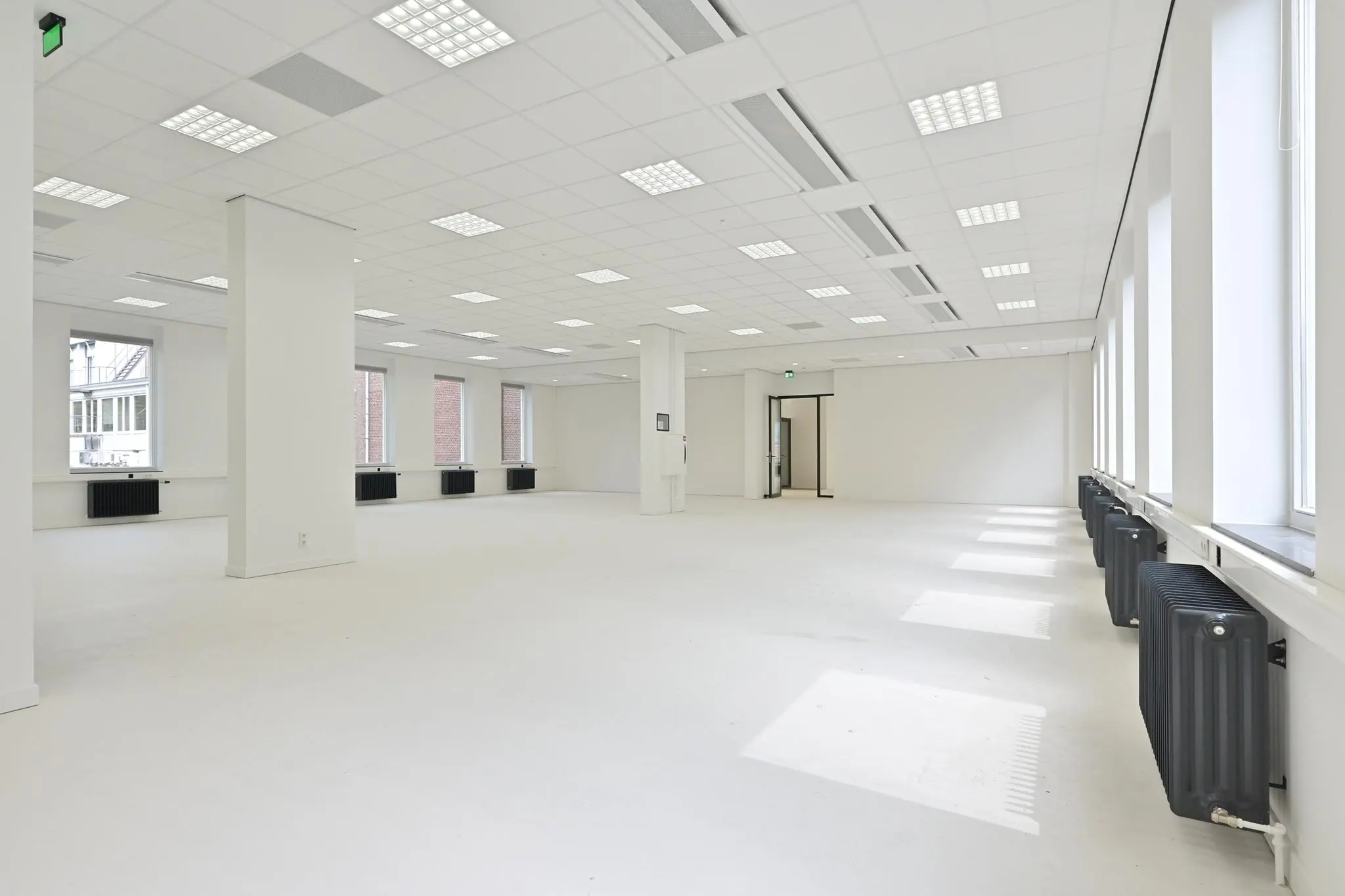 Ruime, lichte kantoorruimte aan de Parkstraat met grote ramen, witte wanden en zwarte radiatoren.