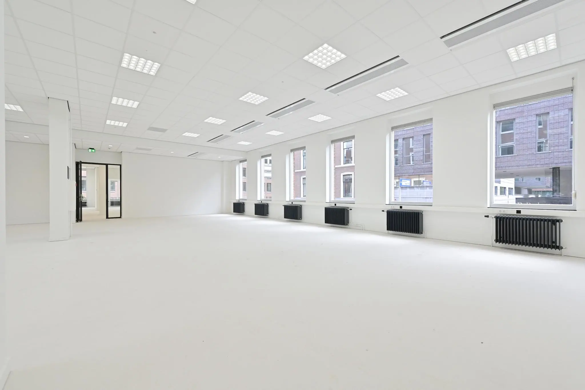 Lichte, lege kantoorruimte aan de Parkstraat met grote ramen en zwarte radiatoren.