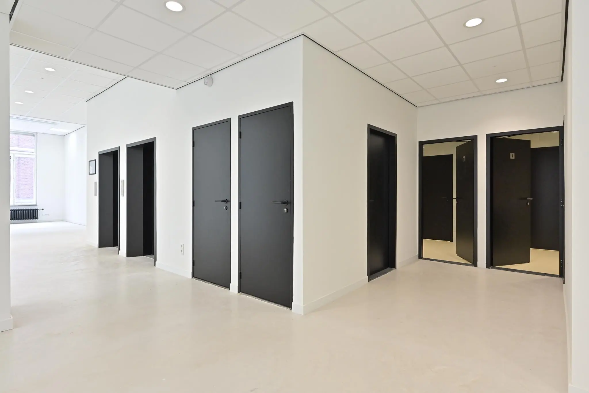 Moderne, witte gang in een kantoorpand aan de Parkstraat met meerdere zwarte deuren en een strakke afwerking.
