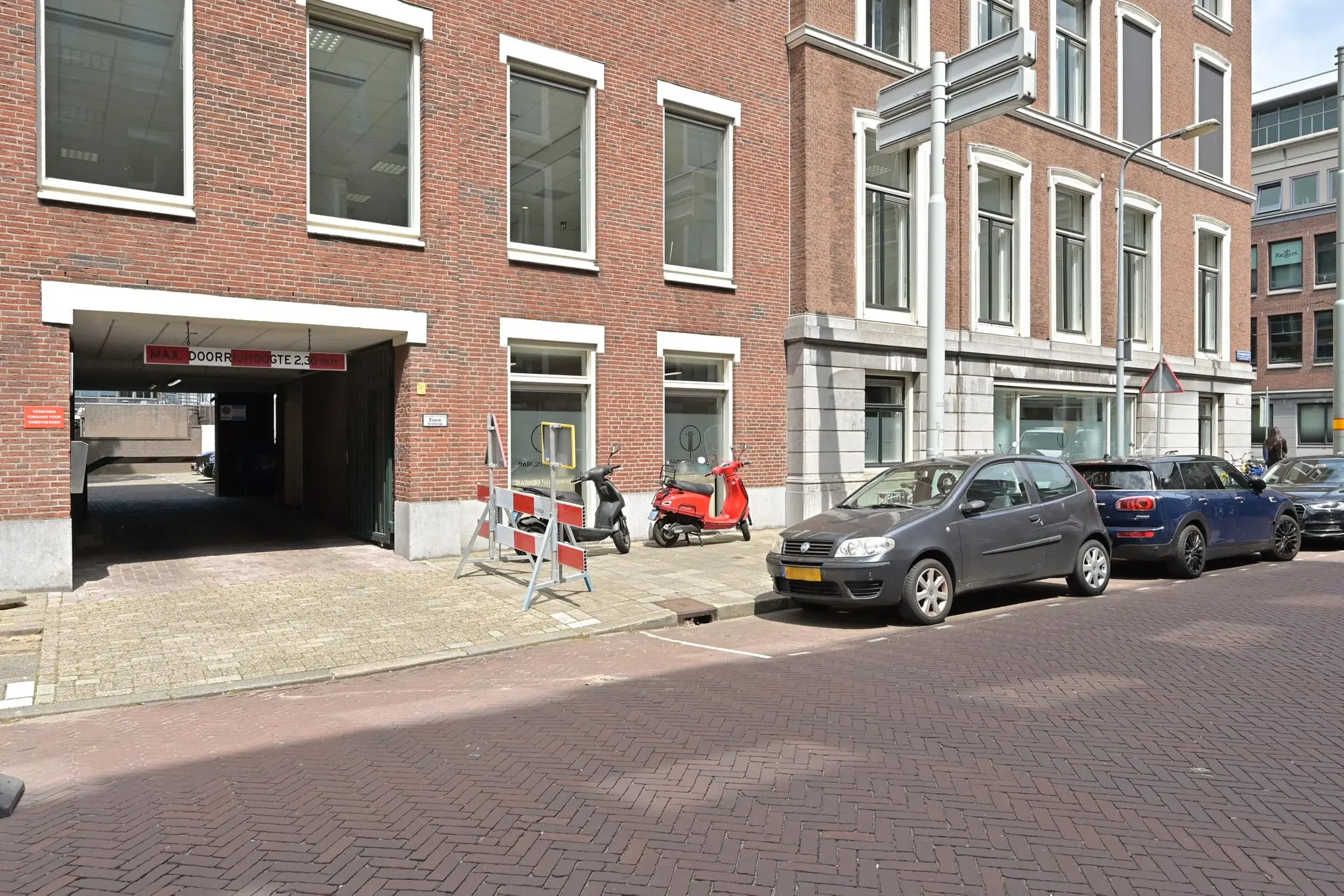 Ingang van een parkeergarage aan de Parkstraat met geparkeerde auto's, scooters en een waarschuwingsbord op de stoep.
