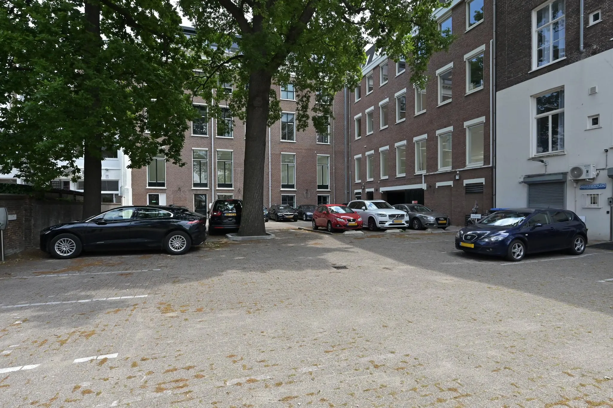 Parkeerplaats aan de Parkstraat omringd door bakstenen kantoorpanden en geparkeerde auto's onder grote bomen.