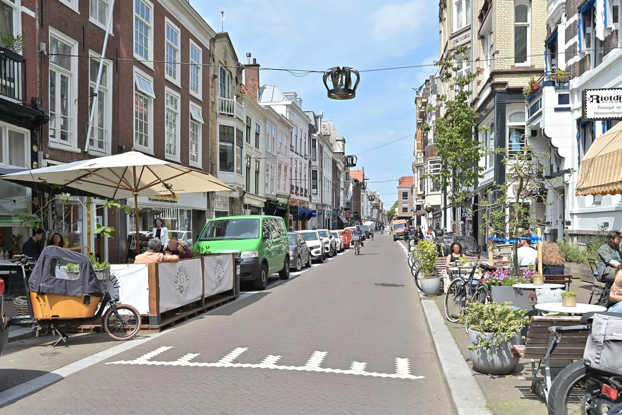 Gezellige winkel- en horecastraat Parkstraat in Den Haag met terrassen, geparkeerde auto's en passerende fietsers op een zonnige dag.