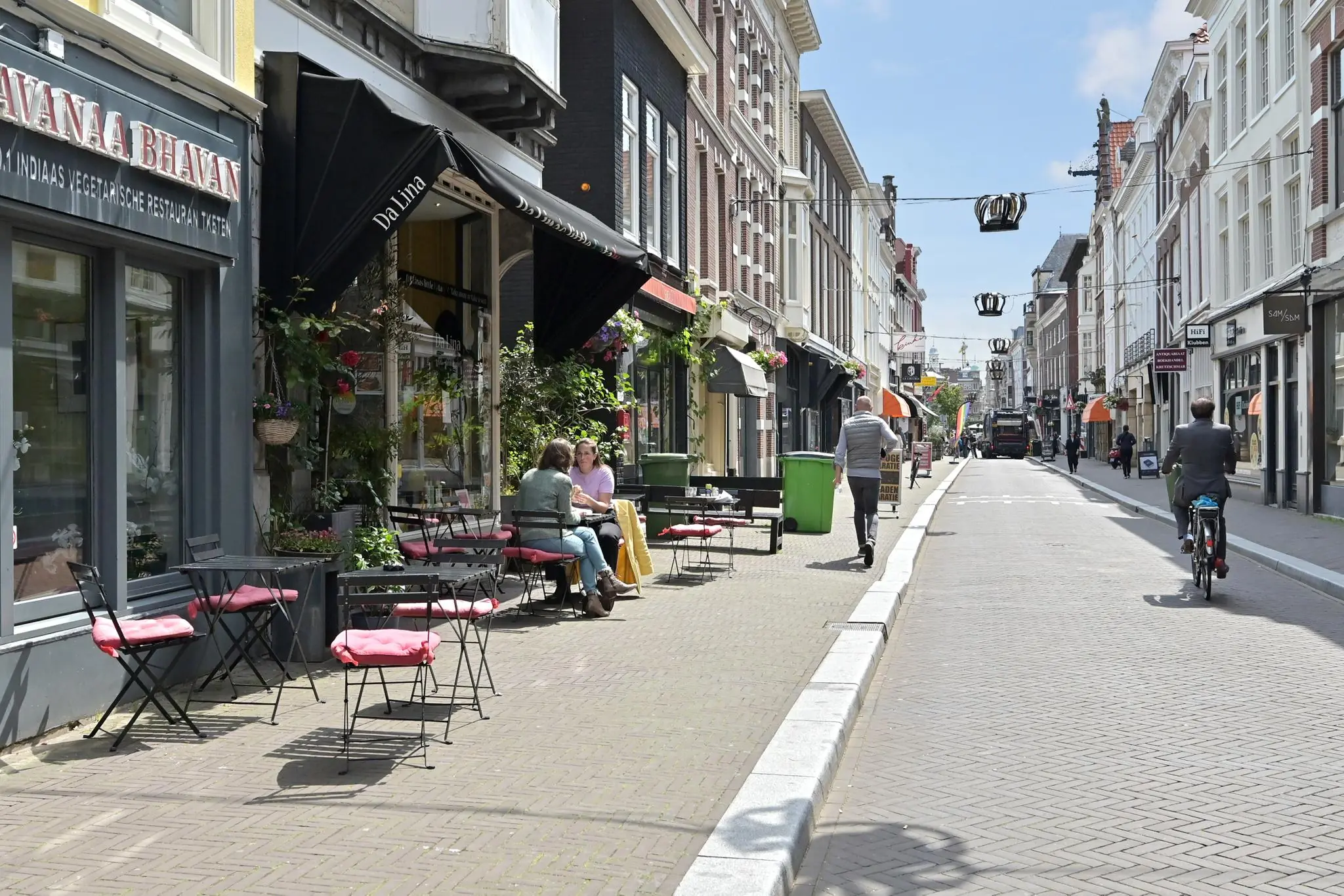 Terras met mensen aan tafel in de zon aan de Parkstraat, omringd door winkels en restaurants.