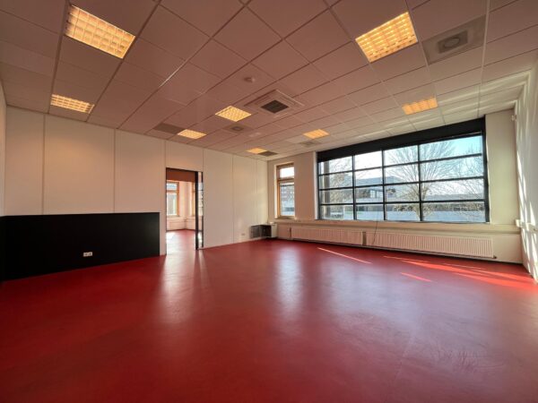 Lichte kantoorruimte met rood vloerzeil, systeemplafond en grote ramen bij Veldzigt.