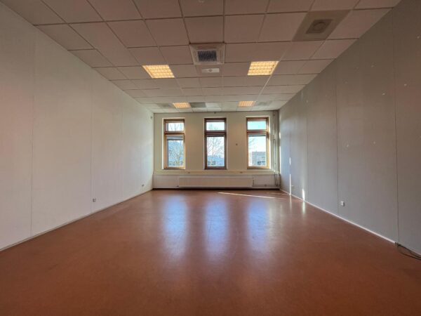 Leeg klaslokaal in Gebouw Veldzigt met drie grote ramen en systeemplafond.