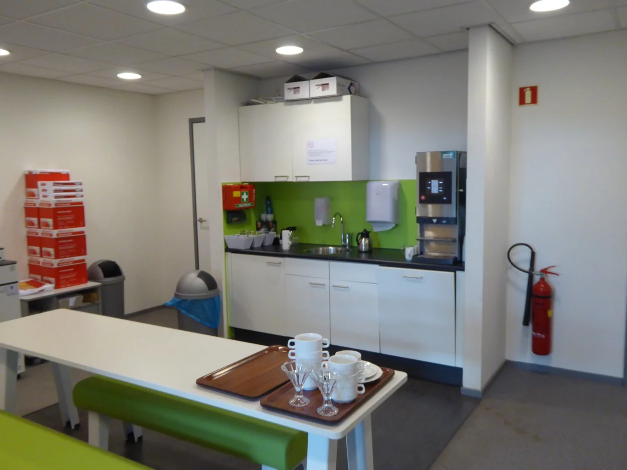 Bedrijfskeuken aan de Maarssenbroeksedijk met koffieautomaat, spoelbak, brandblusser en stapels kantoormateriaal.